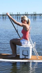 a lady sitting on a hard-sided cooler while paddle boarding